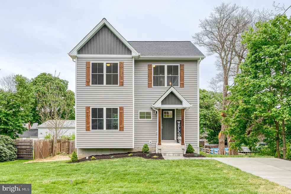 Two-story gray house with wooden shutters, a small front porch, and a vertical 'WELCOME' sign beside the door.