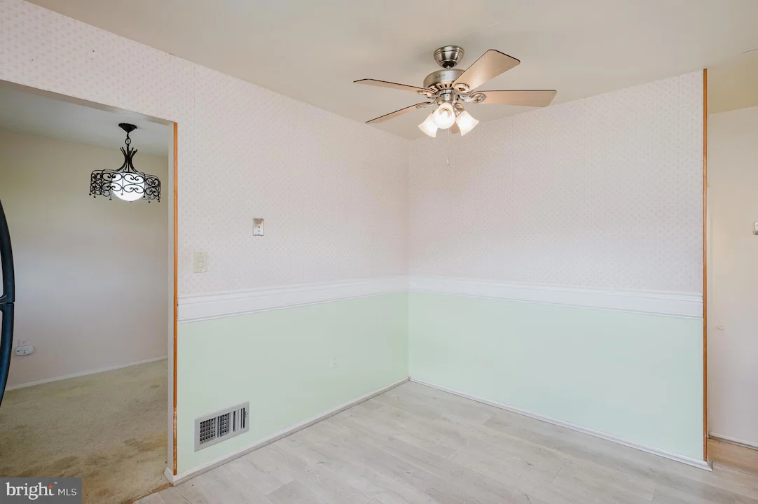 Empty dining nook with pastel wallpaper, mint-green wainscoting, white chair rail, and a silver ceiling fan with lights in the corner of a room.