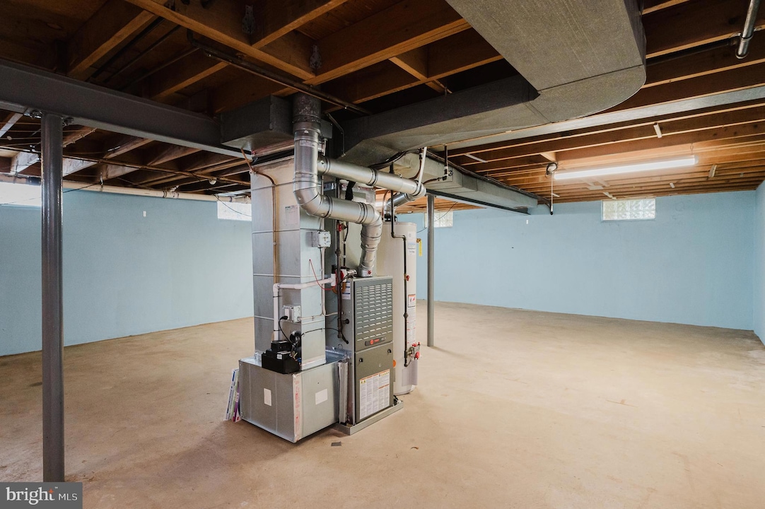 Basement utility area with a furnace and large metal ducts, exposed ceiling beams, and blue walls.