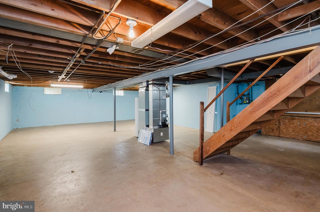 Basement with concrete floor, blue walls, exposed ceiling, and a wooden staircase on the right side leading upstairs.