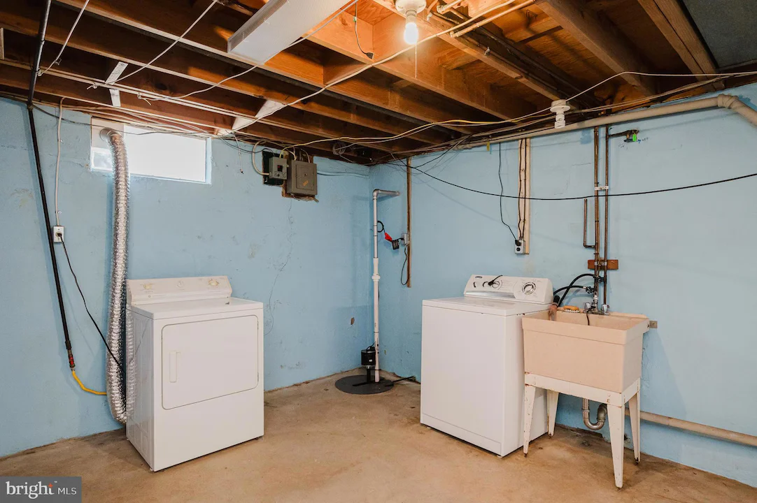 Basement laundry area with a washer, a dryer, and a utility sink against blue walls and exposed ceiling beams.