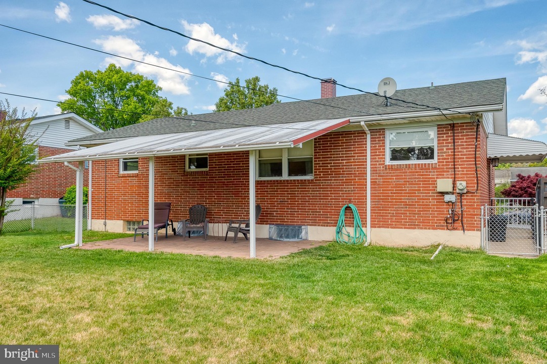 Backyard view of a red brick house with a covered patio and outdoor seating on a brick slab