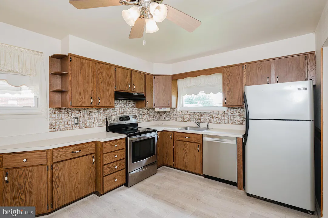 U-shaped kitchen with oak cabinetry, white countertops, stainless steel range and dishwasher, and a large fridge against the right wall.