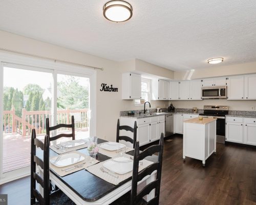 Bright kitchen and dining area with white cabinets, granite countertops, and a table set for four near a sliding glass door to the deck