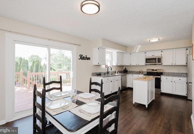 Bright kitchen and dining area with white cabinets, granite countertops, and a table set for four near a sliding glass door to the deck