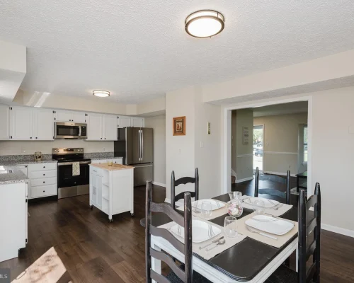 Open-concept kitchen and dining area with white cabinets, stainless steel fridge and range, and a table set for four in the foreground