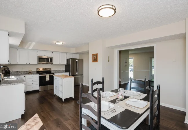 Open-concept kitchen and dining area with white cabinets, stainless steel fridge and range, and a table set for four in the foreground