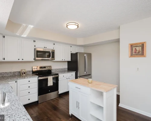 Bright kitchen with white cabinets, granite countertops, stainless steel fridge and range, and a small island with a wood top.