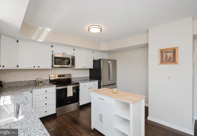 Bright kitchen with white cabinets, granite countertops, stainless steel fridge and range, and a small island with a wood top.