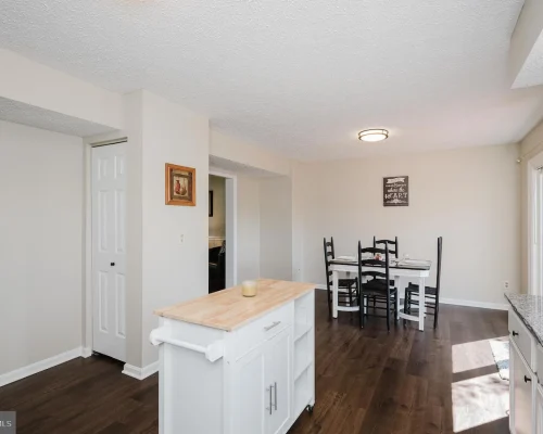 Open kitchen and dining area with a white island, cabinetry, dark wood floor, and a four-seat dining table near a sliding door.