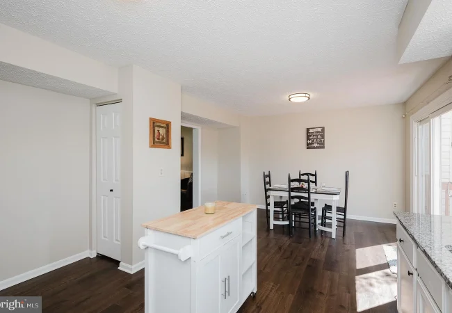 Open kitchen and dining area with a white island, cabinetry, dark wood floor, and a four-seat dining table near a sliding door.