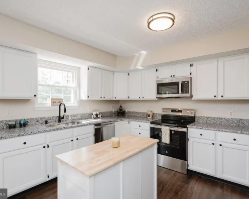 White kitchen with grey speckled countertops, island, and stainless steel appliances including fridge, oven, and microwave.