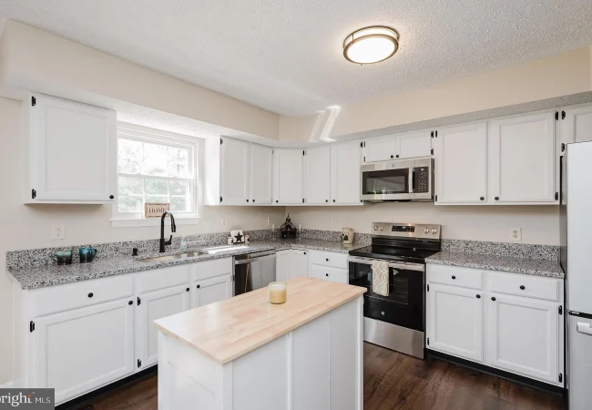 White kitchen with grey speckled countertops, island, and stainless steel appliances including fridge, oven, and microwave.