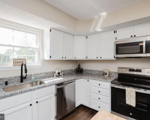Bright, modern kitchen with white cabinets, granite counters, and stainless steel appliances including a dishwasher and range under a microwave.