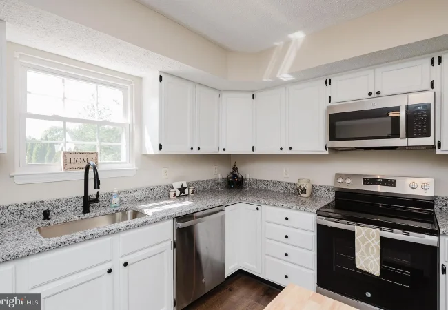 Bright, modern kitchen with white cabinets, granite counters, and stainless steel appliances including a dishwasher and range under a microwave.