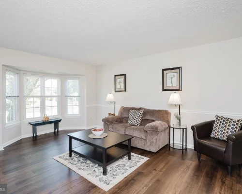 Living room with beige sofa, brown leather chair, coffee table, and bay window area in a bright, neutral decor.