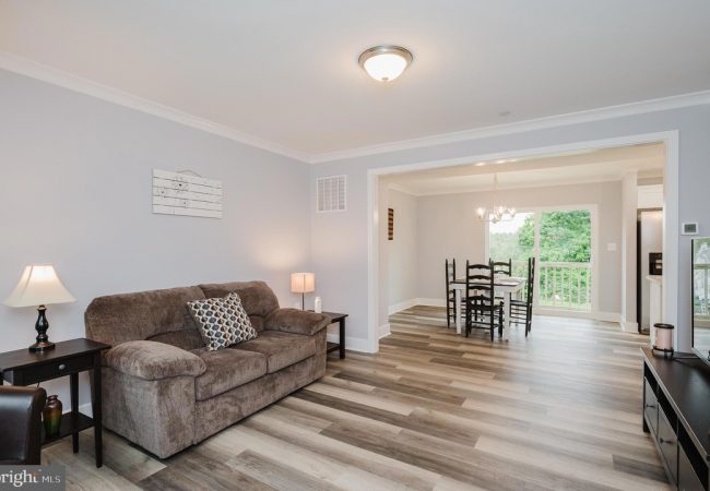 Bright living room with a brown sofa, two side tables with lamps, and an open dining area beyond.