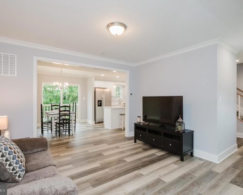 Open-concept living room with gray walls, wood-look flooring, and a black TV stand with a large flat-screen TV.