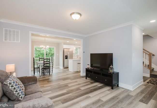 Open-concept living room with gray walls, wood-look flooring, and a black TV stand with a large flat-screen TV.