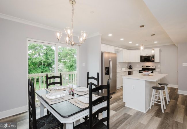 Bright open dining and kitchen area with a white table set for four, black chairs, and a chandelier near a sliding glass door to a green backyard.