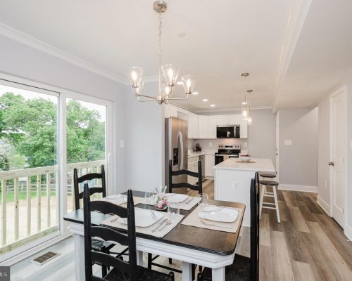 Open-concept kitchen and dining area with a sliding glass door to a deck, white cabinets, stainless steel appliances, and a chandelier over the table.
