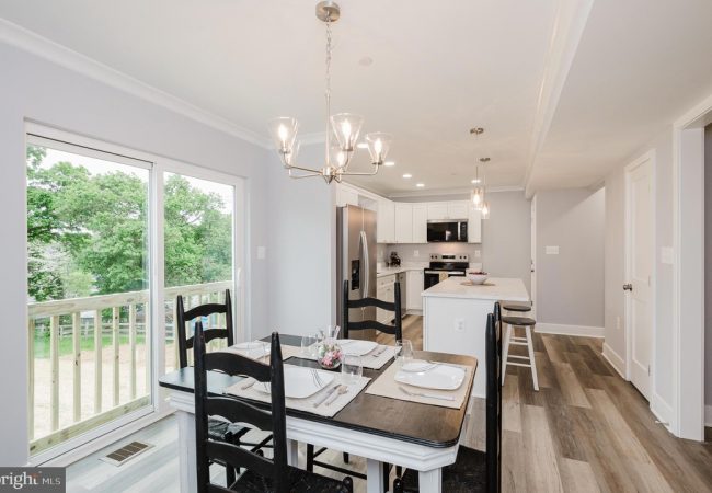 Open-concept kitchen and dining area with a sliding glass door to a deck, white cabinets, stainless steel appliances, and a chandelier over the table.