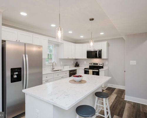 Modern white kitchen with marble island, stainless steel fridge, stove, and pendant lights above the island.