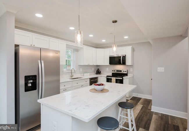 Modern white kitchen with marble island, stainless steel fridge, stove, and pendant lights above the island.