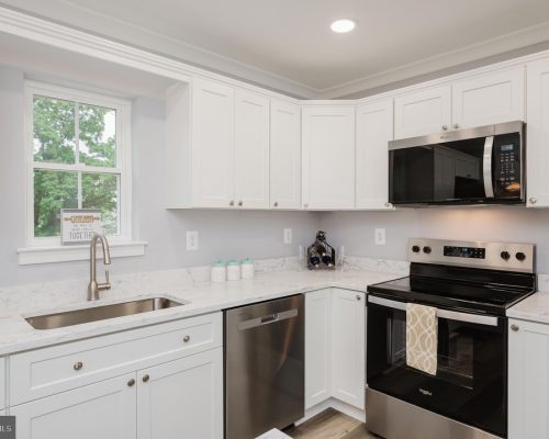 White kitchen with marble countertops, stainless steel appliances, and a window above the sink.