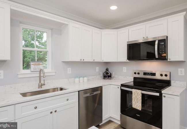 White kitchen with marble countertops, stainless steel appliances, and a window above the sink.