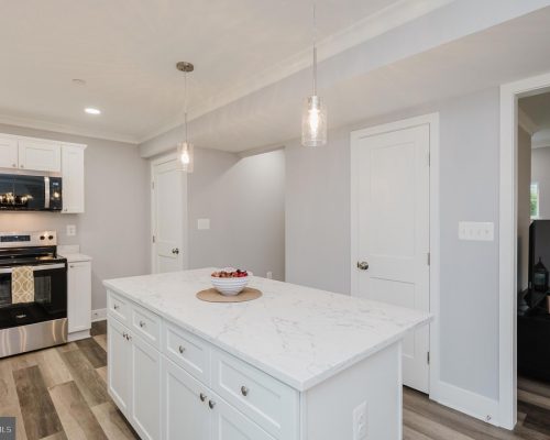 Bright kitchen with a marble-topped island, white cabinets, and pendant lights over the island.
