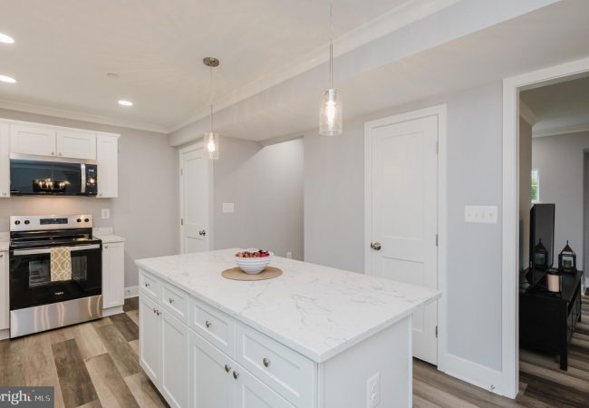 Bright kitchen with a marble-topped island, white cabinets, and pendant lights over the island.