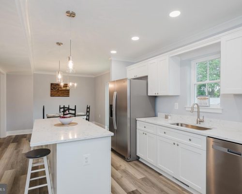 Bright white kitchen with marble island, stainless steel appliances, and a dining nook in the background.