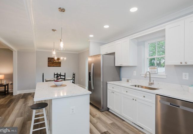 Bright white kitchen with marble island, stainless steel appliances, and a dining nook in the background.