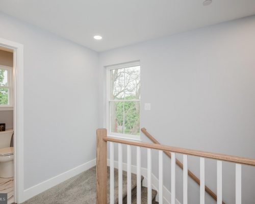 Upstairs landing with a wooden railing, window letting light in, and a small bathroom to the left.