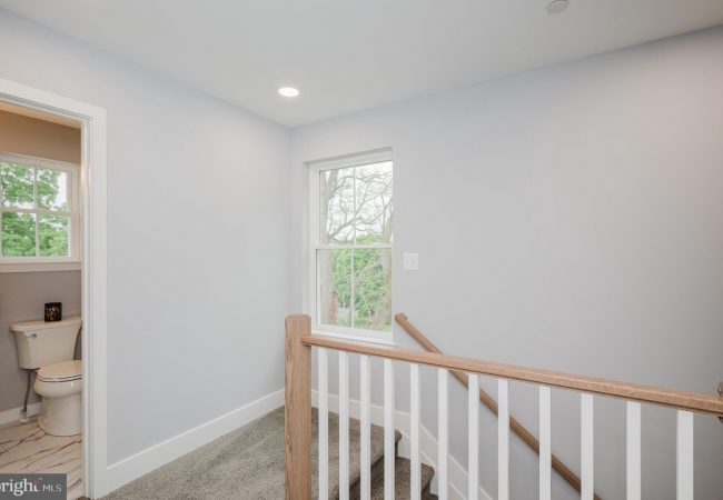 Upstairs landing with a wooden railing, window letting light in, and a small bathroom to the left.