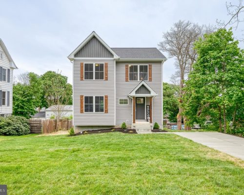 Two-story gray house with brown shutters and a small front porch, a concrete path and manicured lawn leading to the entrance.