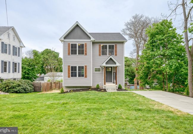 Two-story gray house with brown shutters and a small front porch, a concrete path and manicured lawn leading to the entrance.