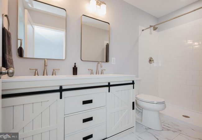 Double-sink bathroom vanity with white cabinets, black hardware, and sliding barn-door drawers, in a light gray room with two rectangular mirrors and brushed-nickel faucets.