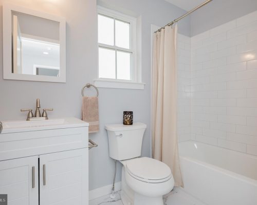 Bright white bathroom with a vanity, mirror, towel ring, toilet, and a bathtub with a beige curtain.