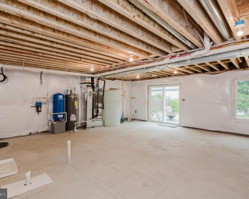 Unfinished basement with exposed ceiling joists, HVAC equipment, water heater, and white plastic vapor barriers along the walls.