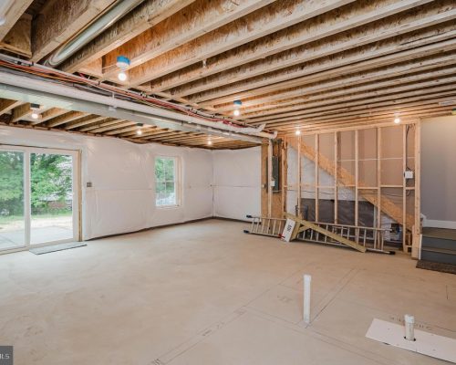 Unfinished basement with exposed joists, plastic-wrapped walls, and a sliding glass door to the outside area.