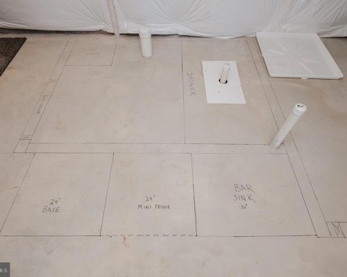 Construction plan on concrete floor showing a bar layout with sections for base (24"), 24" mini fridge, and bar sink (30"), plus plumbing pipes.