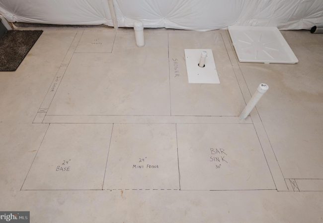 Construction plan on concrete floor showing a bar layout with sections for base (24"), 24" mini fridge, and bar sink (30"), plus plumbing pipes.