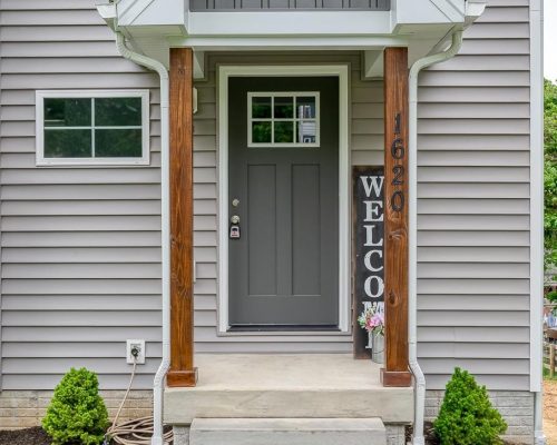 Front entry with gray door, two wooden posts, and a vertical 'WELCOME' sign beside the steps. House number 1620 visible.