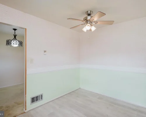 Empty dining nook with pastel wallpaper, mint-green wainscoting, white chair rail, and a silver ceiling fan with lights in the corner of a room.