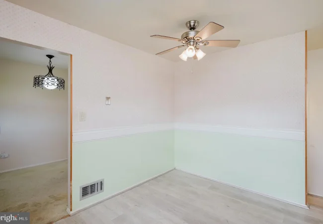 Empty dining nook with pastel wallpaper, mint-green wainscoting, white chair rail, and a silver ceiling fan with lights in the corner of a room.