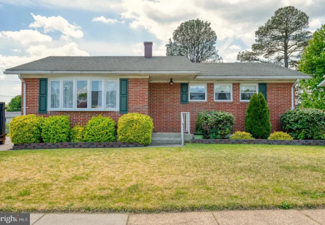 Brick single-story house with green shutters, a gray roof, and a row of trimmed boxwoods in the front yard.