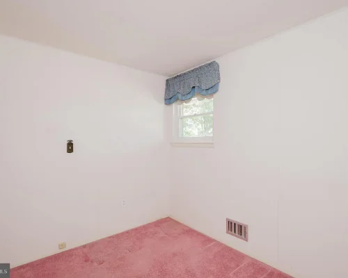 Small empty white room with pink carpet, a single window with blue valance, and a wall vent.