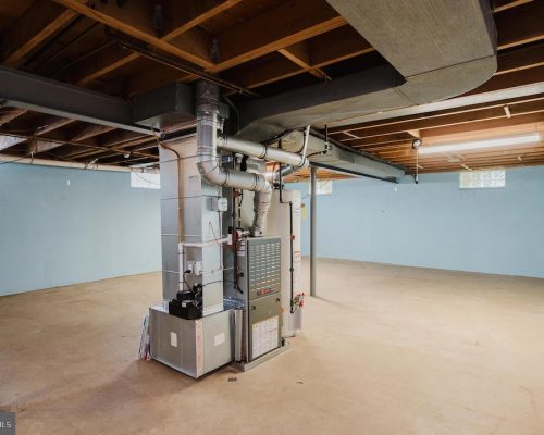 Basement utility area with a furnace and large metal ducts, exposed ceiling beams, and blue walls.